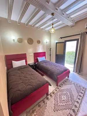 a bedroom with two beds and a rug at Hôtel Zaghro in Ouarzazate