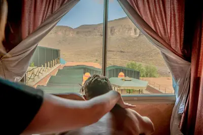 a person sitting in a window looking out at the desert at Ouednoujoum Ecolodge & Spa in Ouarzazate