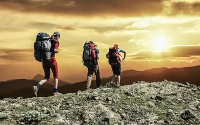 three people with backpacks walking on top of a mountain at Riad Dar Bab Todra in Tinerhir