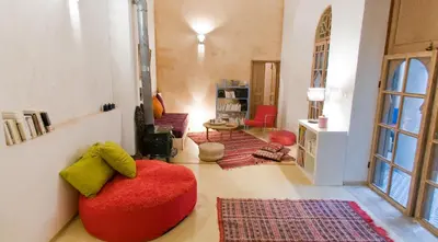 a living room with a red chair in the middle of a room at Riad La Maison D'à Côté in Meknès