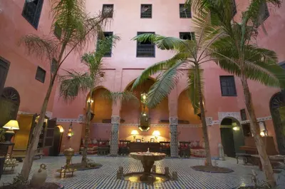 a courtyard with palm trees and a pink building at Dar Anebar in Fès