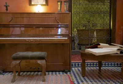 an old piano in a room with a stool and a table at Dar Anebar in Fès