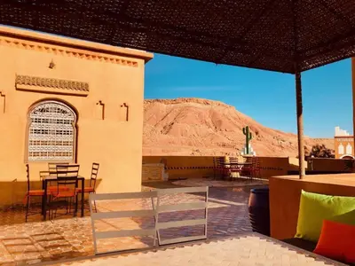 a building with a table and chairs and a mountain at Kasbah Isfoula and spa in Aït Ben Haddou