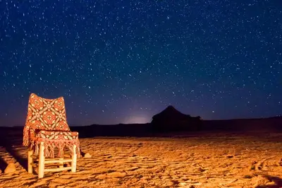 a chair sitting in the desert under a starry sky at Camp Iguidi Tours in Mhamid