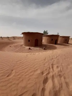 two houses in the desert with footprints in the sand at Camp Iguidi Tours in Mhamid