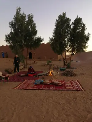 a group of people sitting around a fire in the desert at Camp Iguidi Tours in Mhamid