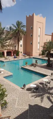 a large swimming pool with palm trees and a building at Hôtel Le Tinsouline in Zagora