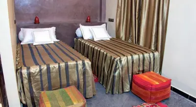 a bedroom with two beds and a stool at Hotel Azoul in Ouarzazate