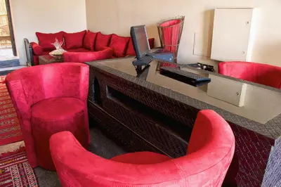 a living room with red chairs and a desk with a television at Hotel Azoul in Ouarzazate