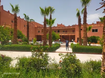 a person walking in front of a building with palm trees at Hotel Mandar Saghrou Tazakhte in Kalaat MGouna