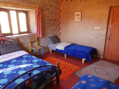 a room with two beds and a chair and a window at Auberge Hostel Traditionnel in Tinerhir