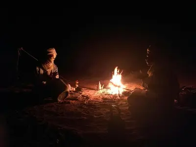 two people sitting around a fire at night at Authentic riad & activities Erg in Mhamid