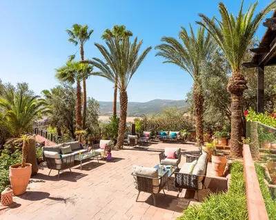 a patio with palm trees and chairs and tables at Widiane Resort in Bine el Ouidane