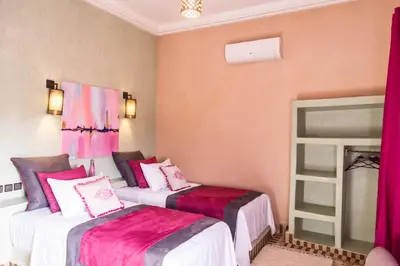 two beds in a room with pink curtains at Riad Azawad in Merzouga