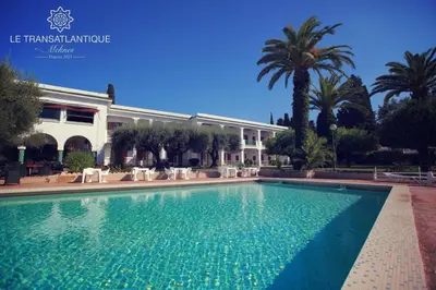 a swimming pool in front of a building with palm trees at Hotel Transatlantique in Meknès
