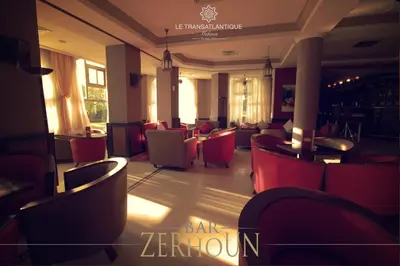 a restaurant with red chairs and a bar at Hotel Transatlantique in Meknès