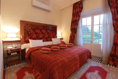 a bedroom with a red bed with two pillows on it at Hotel Transatlantique in Meknès
