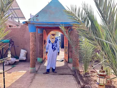 a woman standing in front of a small building at Auberge L'Oasis Mhamid in Mhamid