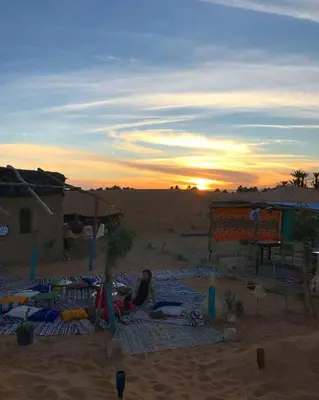 a woman sitting on a blanket in the desert at sunset at SaharaTime Camp in Hassilabied