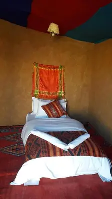 a bedroom with a bed with an orange blanket at SaharaTime Camp in Hassilabied