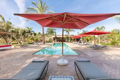 a pool with a red umbrella and two lounge chairs and a pool at Villa Koutoubia, jardin luxuriant, piscine et spa in Marrakech