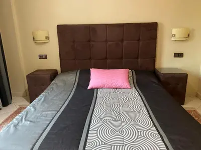 a bed with a brown headboard and a pink pillow at Hôtel Atlas Guercif in Guercif