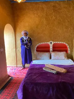 a woman standing next to a bed in a room at Dar Yaya in Mhamid