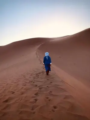 a man walking down a sand dune in the desert at Dar Yaya in Mhamid