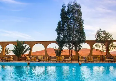 a pool at a desert resort with chairs and trees at Palmeras Y Dunas Luxery Camp in Merzouga
