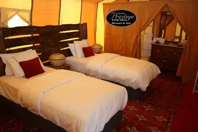 a bedroom with two beds with white sheets and red pillows at Karim Sahara Prestige in Zagora