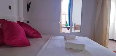 a white bed with red pillows and a window at Riad Bleu Afriqua in Boumalne