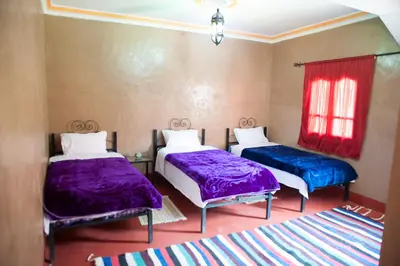two beds in a room with purple sheets and a window at Les Jardins De Todgha gorges de todra tinghir in Aït Baha