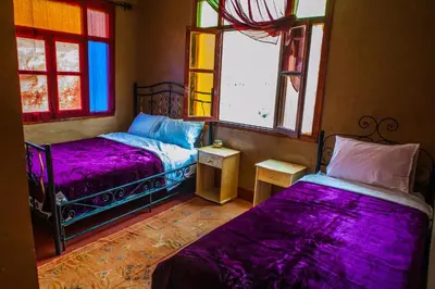 a bedroom with two beds with purple sheets and windows at Les Jardins De Todgha gorges de todra tinghir in Aït Baha