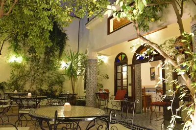 an outdoor patio with tables and chairs and trees at Riad Jardin Chrifa in Fès