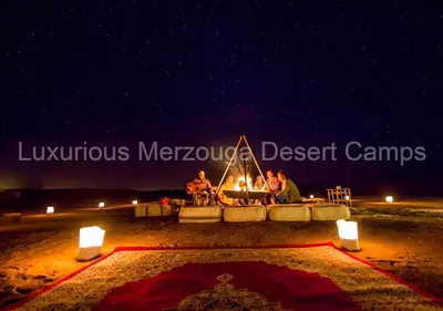a group of people sitting around a fire in the desert at Luxurious Merzouga Desert Camps in Merzouga