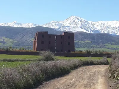 a building on a dirt road with mountains in the background at Kasbah ATFEL in Ourika
