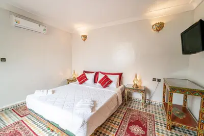 a bedroom with a white bed with red pillows and a tv at Riad Taj Salma in Fès