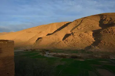 a mountain in the middle of a desert with a green field at Hotel Baddou in Tamtetoucht