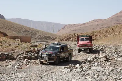 two trucks and a red truck on a rocky road at Hotel Baddou in Tamtetoucht