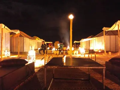 a group of tents at night with a table at Merzouga Luxury Bivouac in Merzouga