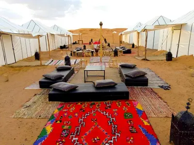 a group of tents with a rug in the desert at Merzouga Luxury Bivouac in Merzouga