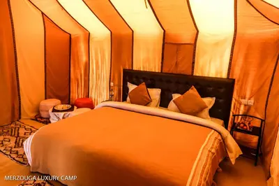 a bedroom with a bed with orange sheets and pillows at Merzouga Luxury Bivouac in Merzouga