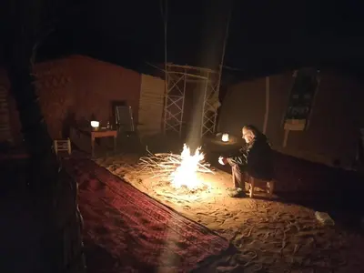 a man sitting around a fire at night at Obira Oasis Merzouga Camp in Merzouga