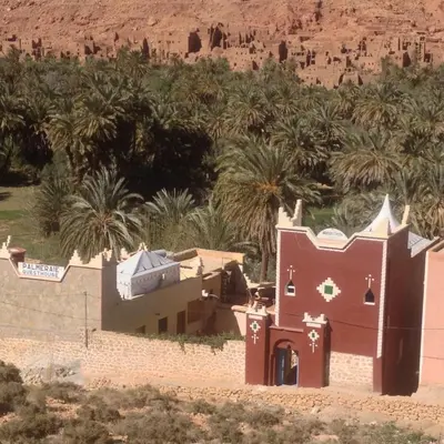 a house in the desert with palm trees in the background at Palmeraie Guest House in Tinerhir