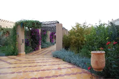 a garden with a brick walkway and an arch with flowers at Auberge Tinit in Er Rachidia