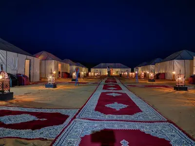 a row of tents with red and white carpets on the ground at Ammar Luxury Camp in Merzouga