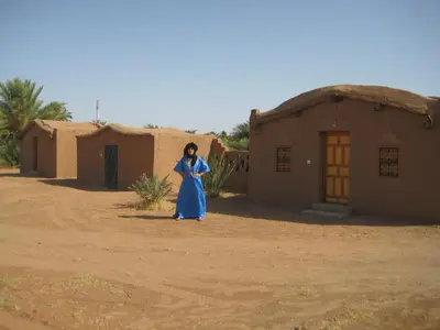 a woman in a blue dress standing in front of a building at Camping Les Palmeraies - Oasis Escape Tagounite in Tagounite