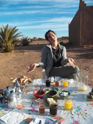 a woman sitting in front of a table of food at Camping Les Palmeraies - Oasis Escape Tagounite in Tagounite