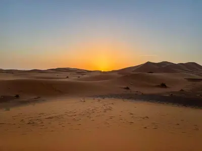 a sunset in the desert with the sun in the distance at Desert Camp Erg Chebbi in Merzouga