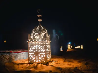 a lit up lantern sitting in the sand at night at Desert Camp Erg Chebbi in Merzouga